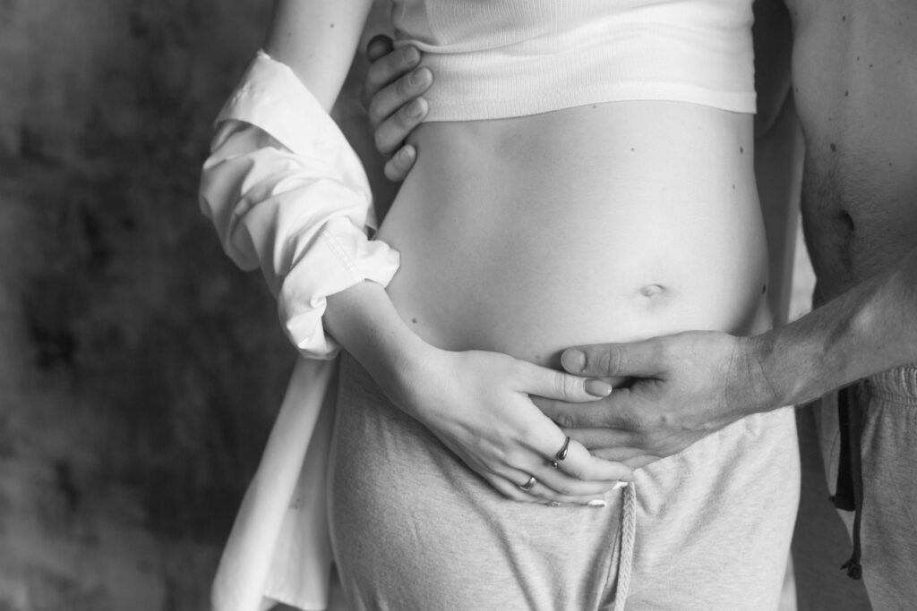 A black and white photograph of expectant parents gently cradling a pregnant belly, symbolizing the delicate considerations of cannabis use during pregnancy.
